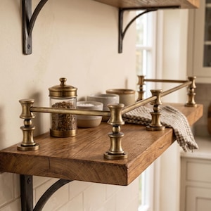 May include: A thick wooden shelf mounted with dark metal brackets, featuring a brass railing along the front and sides. On the shelf sits a clear glass jar with a brass lid containing spices, two small ceramic bowls, and a folded checkered cloth.