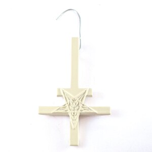 May include: A white ceramic upside-down cross with a pentagram in the center. The cross has a hook at the top for hanging.