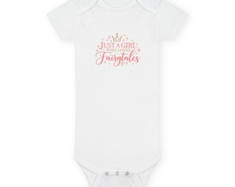 May include: A white short-sleeved baby bodysuit featuring a gold crown icon above the pink and gold text that reads Just A Girl Who Loves Fairytales, accented with small star shapes and a tiny heart, with three metal snaps at the bottom.
