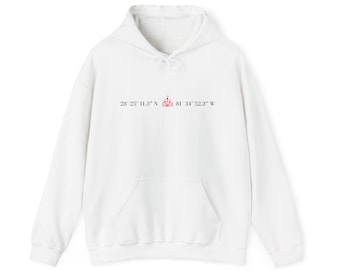 May include: A white long-sleeve hooded sweatshirt featuring a front kangaroo pocket and a drawstring hood. The chest displays the text 28° 25' 11.3" N 81° 34' 52.3" W with a small pink castle icon centered between the coordinates.