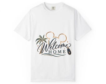 May include: A white short-sleeve t-shirt featuring a graphic design with a copper-colored Mickey Mouse ear outline, a palm tree, and the text "Welcome HOME" in dark blue script and block lettering, accompanied by a small dark blue luggage tag.