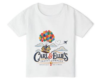 May include: A white short-sleeve t-shirt featuring a graphic of a yellow house lifted by a cluster of colorful balloons. Below the house, the text reads Carl & Ellie's Travel Company, with the tagline Adventures Big & Small and a small airplane.