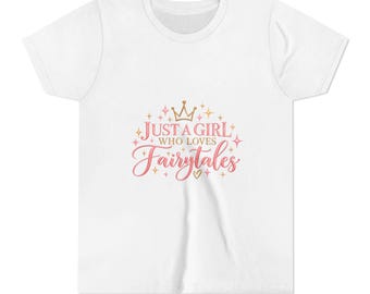 May include: A white short-sleeved t-shirt featuring a graphic print in pink and gold. The text reads Just a Girl Who Loves Fairytales, accompanied by a crown icon, small sparkling star shapes, and a tiny heart symbol centered on the chest.