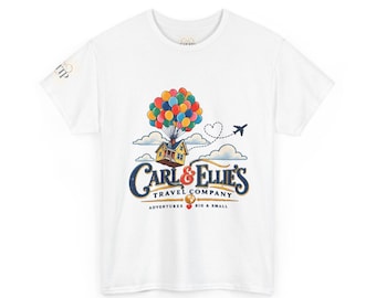 May include: A white short-sleeve t-shirt featuring a graphic of a house lifted by colorful balloons. The text reads Carl & Ellie's Travel Company Adventures Big & Small. A small airplane and heart-shaped flight path are visible above the house.