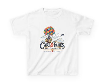 May include: A white short-sleeve t-shirt featuring a graphic of a house lifted by colorful balloons. The text reads Carl & Ellie's Travel Company Adventures Big & Small, accompanied by a small airplane and a dotted heart-shaped flight path.