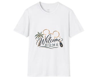May include: A white short-sleeve t-shirt featuring a graphic design with the text "Welcome Home" in dark blue script and block lettering. The design includes a gold-outlined mouse ear silhouette, a palm tree, and a small luggage tag icon.