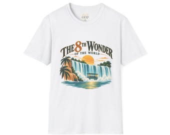 May include: A white short-sleeve t-shirt featuring a graphic print of a waterfall, palm trees, and a boat under a setting sun. The text "THE 8TH WONDER OF THE WORLD" is printed in a dark, arched font above the illustration on the center of the chest.