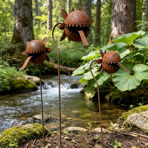 May include: Three garden stakes made of rusted metal, each featuring a spherical head with jagged, triangular teeth and a protruding tongue. The heads are attached to thin, vertical metal rods, creating a set of three plant-like sculptures.