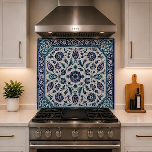 Può includere: Una cappa aspirante e un piano cottura a gas in acciaio inossidabile davanti a un paraschizzi decorativo con un motivo floreale simmetrico nei toni del blu, bianco e rosso. La cucina include armadi bianchi e un tagliere in legno.