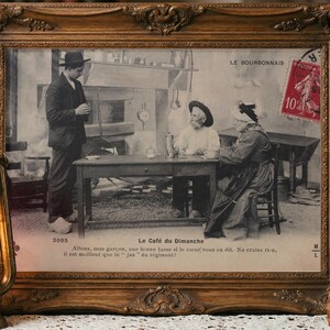 May include: A vintage black and white postcard titled Le Café du Dimanche in an ornate gold frame. It depicts a man standing before a seated couple at a table. A red 10 centime postage stamp is in the top right corner. The text reads Allons, mon garçon.