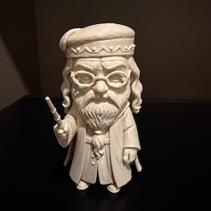 May include: A cream-colored figurine of a wizard with a long white beard, glasses, and a hat. The wizard is holding a wand and wearing a long coat. The figurine is standing on a black surface.