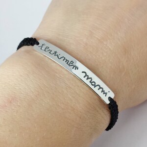 May include: A black cord bracelet with a silver bar charm that reads "I love you Mom".