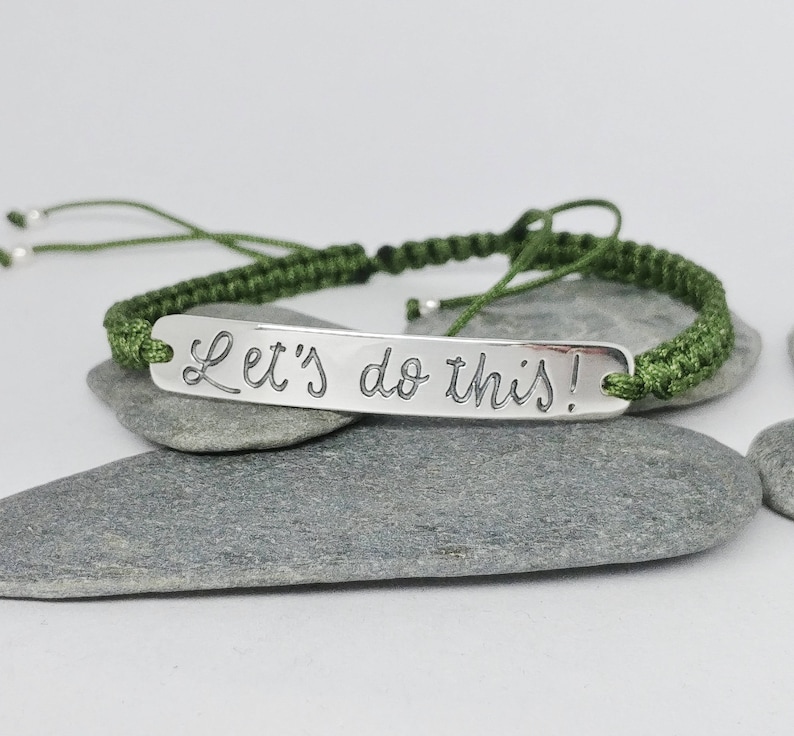 May include: A green cord bracelet with a silver charm that reads "Let's do this!"