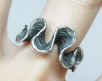 May include: A silver ring with a wavy, organic design. The ring is made of a textured metal and has a unique, modern look.