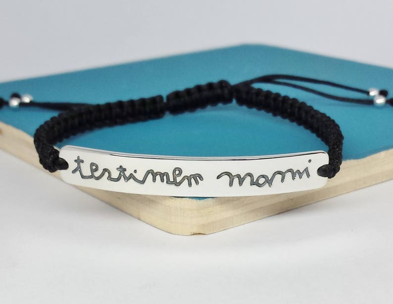 May include: Black braided bracelet with a silver bar charm engraved with the words "terribile mammi".