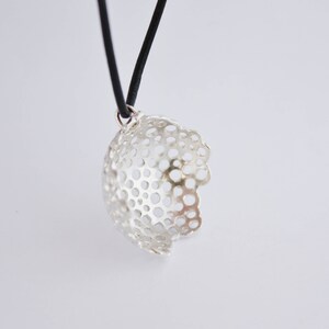 May include: A silver pendant necklace with a delicate, openwork design. The pendant is shaped like a sphere with a circular pattern of holes. The necklace is on a black cord.