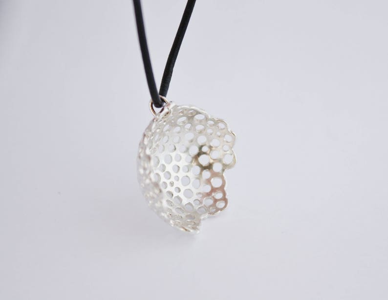 May include: A silver pendant necklace with a delicate, openwork design. The pendant is shaped like a sphere with a circular pattern of holes. The necklace is on a black cord.