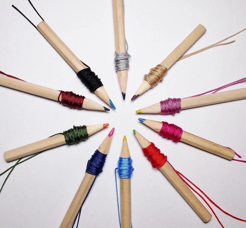 May include: A collection of wooden pencils with colorful string wrapped around the ends. The pencils are arranged in a starburst pattern on a white background.