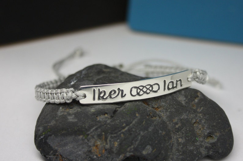 May include: A silver bracelet with a gray cord and a silver tag that says "Iker &infin; Ian".