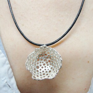 May include: A silver necklace with a delicate, openwork pendant shaped like a sphere. The pendant has a circular pattern of small holes throughout. The necklace is on a black cord.