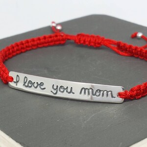 May include: Red string bracelet with a silver charm that says "I love you mom".
