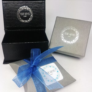 May include: A gray and blue gift box with a blue ribbon. The box has a white label with the text "Tere Reyes Jewelry" on it.