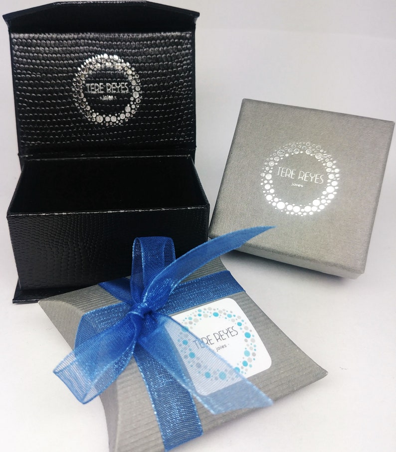 May include: A gray and blue gift box with a blue ribbon. The box has a white label with the text "Tere Reyes Jewelry" on it.
