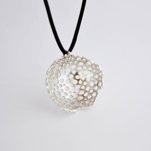 May include: A silver pendant necklace with a delicate, openwork design resembling a flower. The pendant is suspended from a black cord.