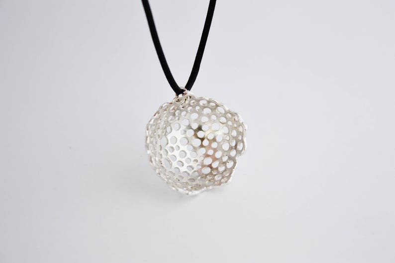 May include: A silver pendant necklace with a delicate, openwork design resembling a flower. The pendant is suspended from a black cord.