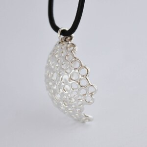 May include: A silver pendant necklace with a delicate, intricate design of interconnected circles. The pendant is suspended from a black cord.