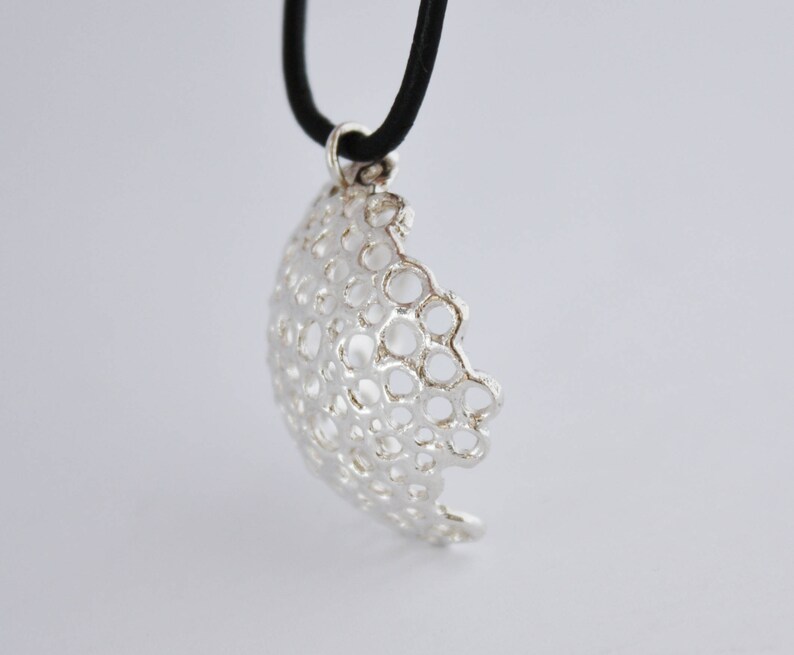 May include: A silver pendant necklace with a delicate, intricate design of interconnected circles. The pendant is suspended from a black cord.