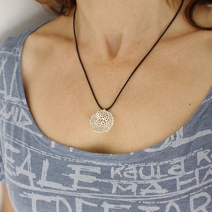 May include: A silver pendant necklace with a delicate, intricate, geometric design. The pendant is suspended from a black cord.