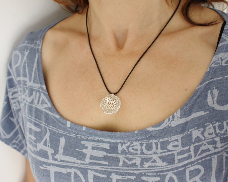 May include: A silver pendant necklace with a delicate, intricate, geometric design. The pendant is suspended from a black cord.