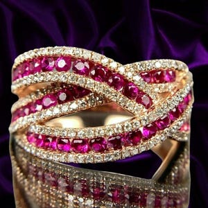 May include: A rose gold ring featuring a crisscross design with multiple rows of round-cut vibrant pink rubies and small white diamonds. The band is constructed with intertwined metal strands, creating a layered appearance with sparkling gemstones.