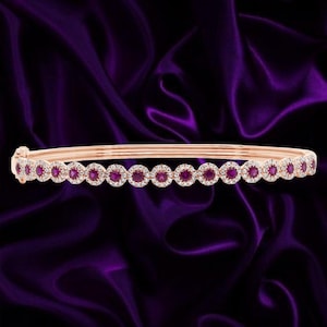 Peut inclure: Un bracelet jonc en or rose composé d'une rangée continue de sertissages circulaires, chacun contenant une pierre précieuse rouge ronde entourée d'un halo de petites pierres blanches étincelantes, avec un fermoir à charnière.