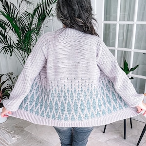 Peut inclure: Un cardigan en crochet de couleur lilas clair et turquoise avec un motif en losanges. Le cardigan est tenu ouvert pour montrer le dos.