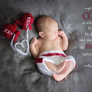 May include: A newborn baby boy wearing a white and red knitted boxing outfit, sleeping on a gray textured surface.  Two red knitted boxing gloves are on the surface, connected by a white string with a heart shape. The text "COURAGE is asking for a time out To Shed A Tear to dust yourself off and then get back into the ring to FIGHT like you've never fought before ~unknown brianak" is on the right side of the image.