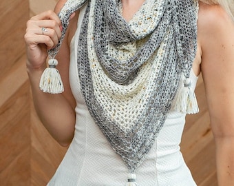 May include: A white and gray crocheted shawl with a fringe trim and tassels. The shawl is draped around a person's neck and shoulders.
