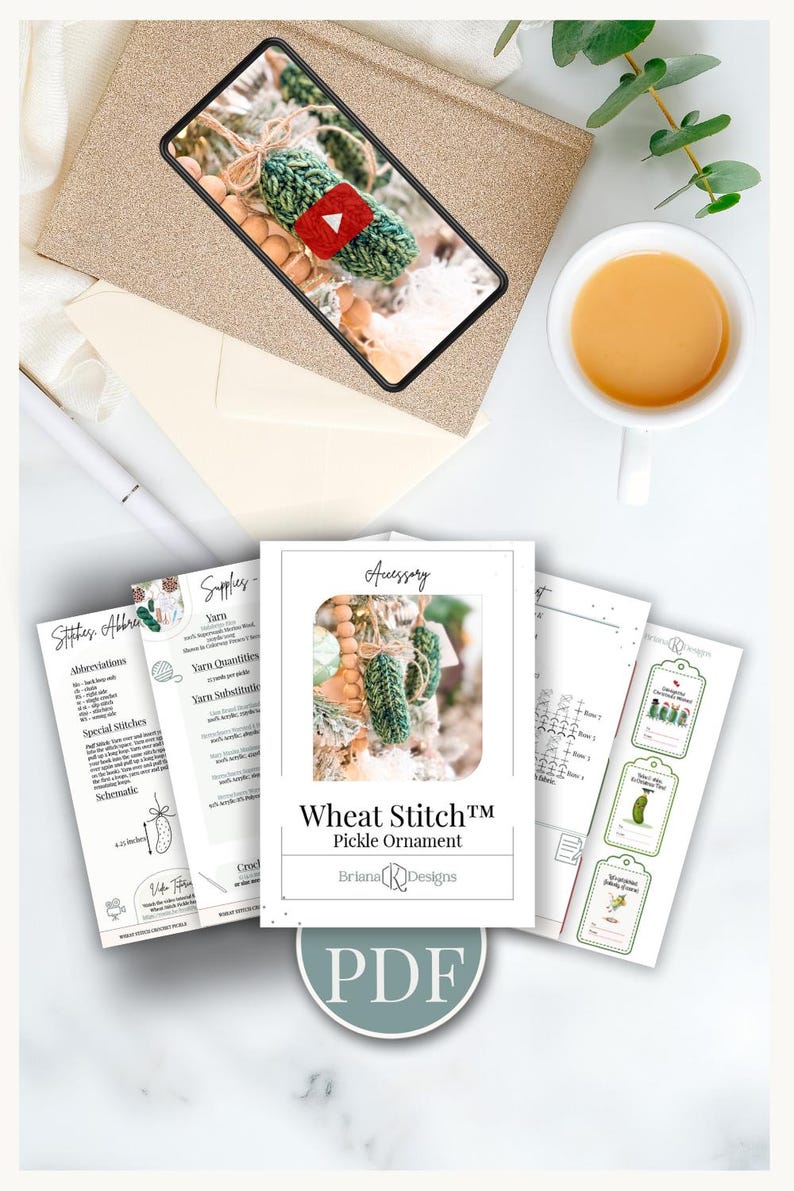 May include: A digital PDF pattern for a Wheat Stitch Pickle Ornament by Briana K Designs, featuring printed pages with crochet instructions, abbreviations, supply lists, and gift tags, displayed alongside a tablet showing a video tutorial.