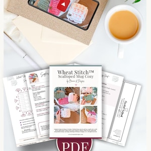May include: An overhead shot features a collection of crochet patterns and supplies. A phone displays a video of colorful crochet mug cozies. The main pattern is titled "Wheat Stitch Scalloped Mug Cozy" and includes a PDF download. A cup of tea sits nearby.