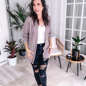 Woman in a casual outfit with ripped jeans and a handmade crochet cardigan standing in a stylish home interior.
