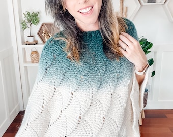 May include: A woman wearing a green and white ombre knitted poncho with a cable knit pattern.