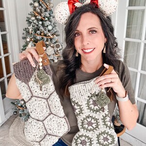 May include: Two handmade crochet Christmas stockings featuring a hexagonal granny square pattern in cream, olive green, and dark brown yarn. Each stocking includes a brown leather hanging loop, wooden beads, and a small decorative crochet charm.