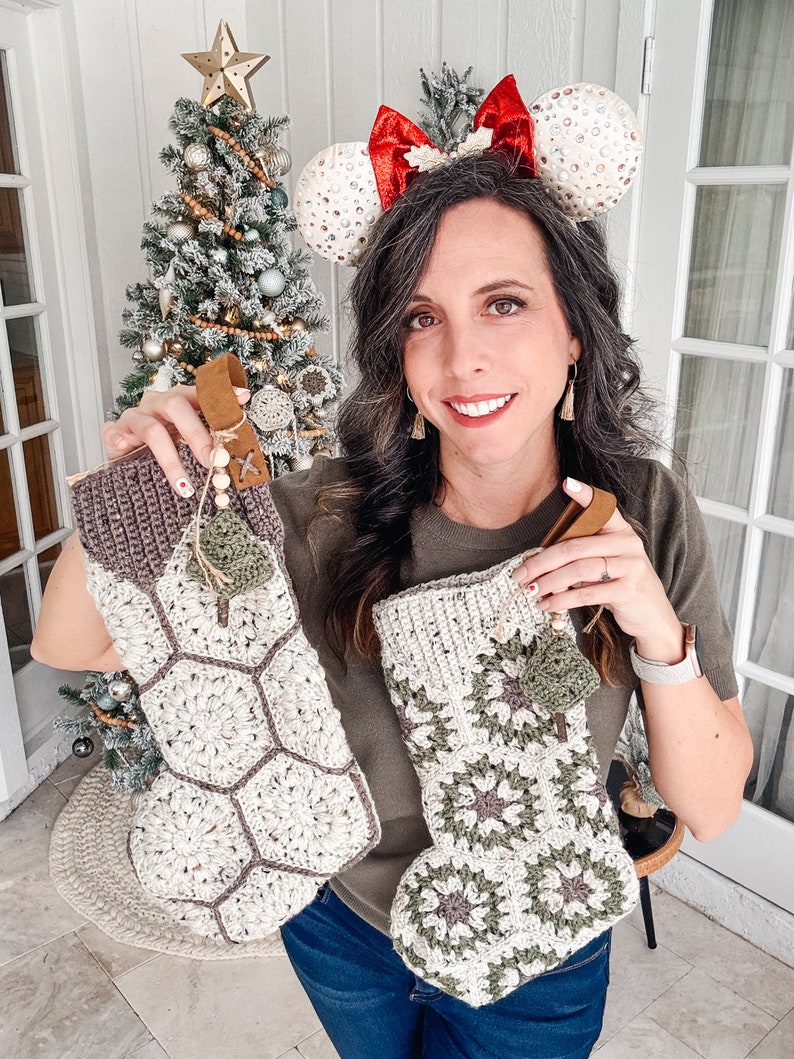 May include: Two handmade crochet Christmas stockings featuring a hexagonal granny square pattern in cream, olive green, and dark brown yarn. Each stocking includes a brown leather hanging loop, wooden beads, and a small decorative crochet charm.