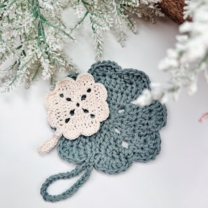 Handcrafted crochet coasters in soft pastel shades, adorned with a flower design, presented on a neutral background with delicate white floral accents, making an exquisite handmade gift.