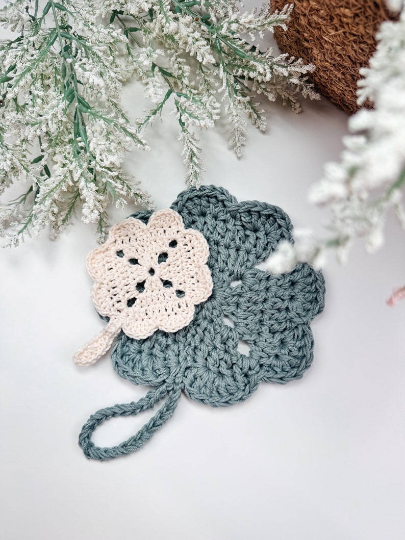 Handcrafted crochet coasters in soft pastel shades, adorned with a flower design, presented on a neutral background with delicate white floral accents, making an exquisite handmade gift.