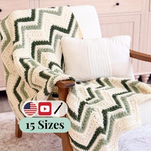 May include: A crochet blanket featuring a chevron pattern in alternating stripes of cream, sage green, and dark forest green. The blanket is draped over a wooden chair with a white rectangular pillow. A label displays the text 15 Sizes.