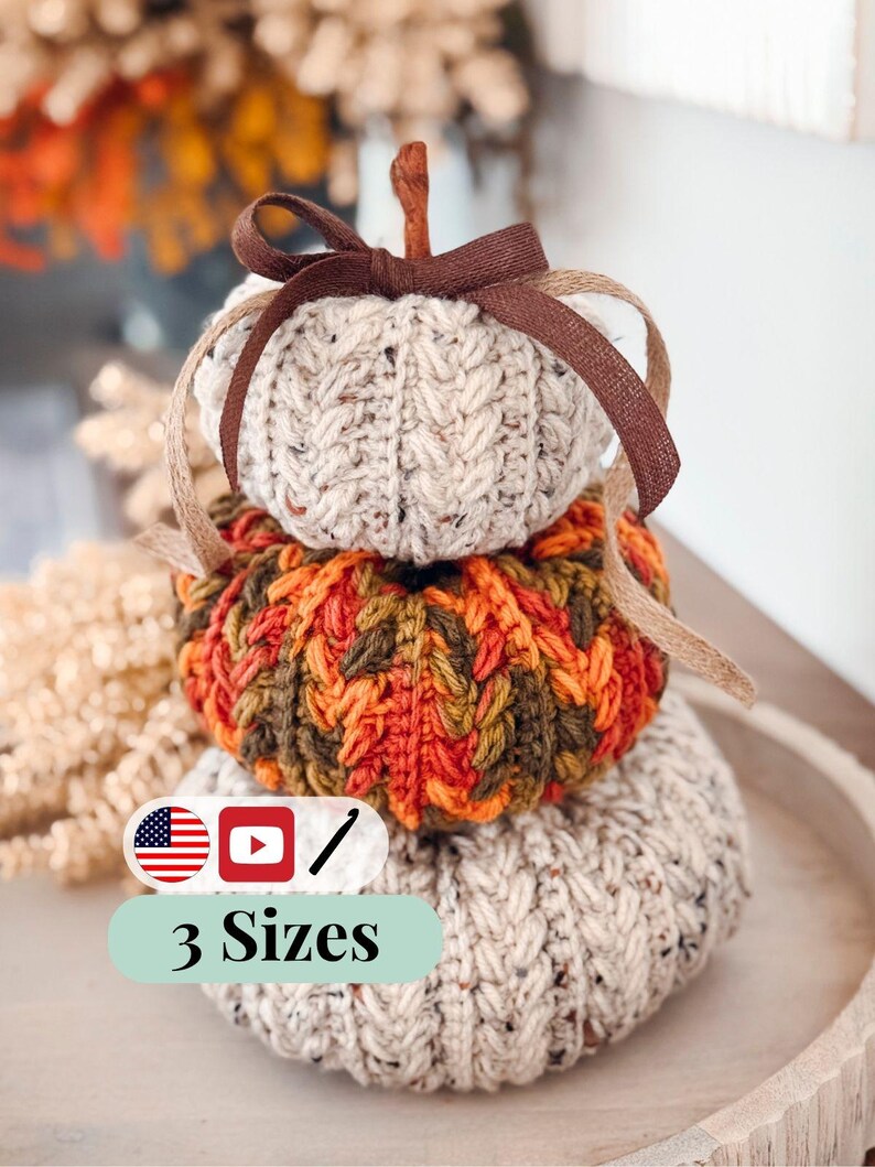 Three stacked crochet pumpkins in speckled oatmeal and orange-green with braided texture and a brown ribbon bow