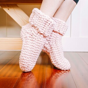 May include: A pair of pink knitted slipper socks with a folded cuff. The socks are made with a soft, chunky yarn and have a simple, cosy design.