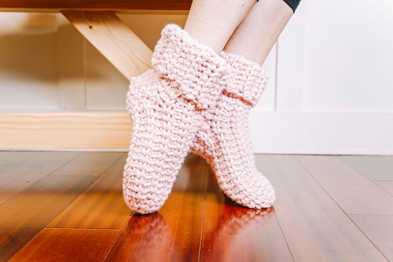 May include: A pair of pink knitted slipper socks with a folded cuff. The socks are made with a soft, chunky yarn and have a simple, cosy design.